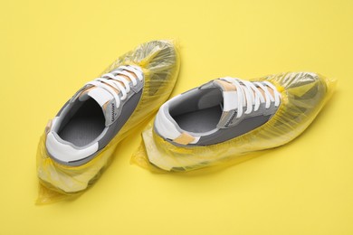 Sneakers in shoe covers on yellow background, closeup