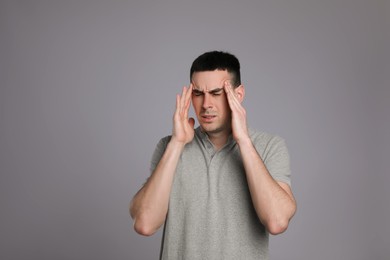Photo of Young man suffering from headache on grey background, space for text. Cold symptoms