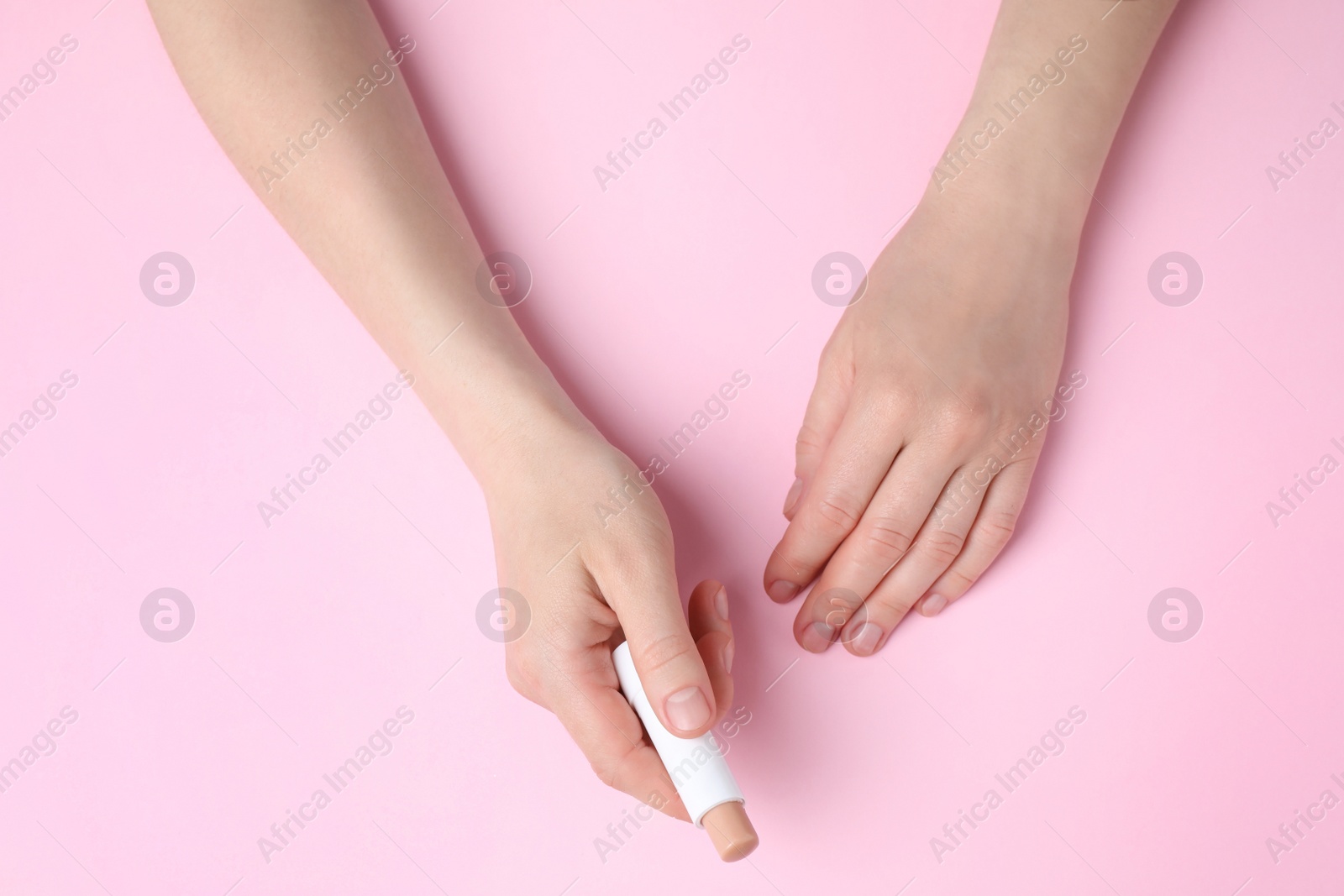 Photo of Woman holding hygienic lipstick on pink background, top view