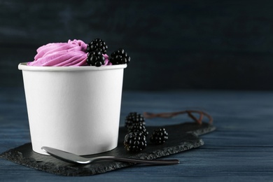 Photo of Cup with tasty frozen yogurt and blackberries on blue wooden table. Space for text