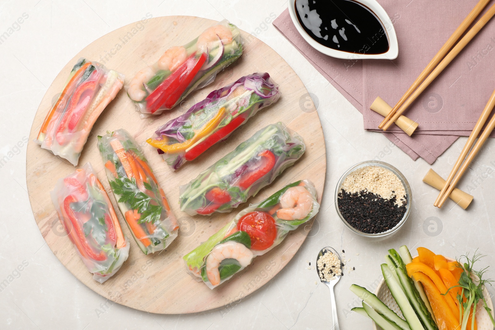 Photo of Delicious rolls wrapped in rice paper served on light table, flat lay