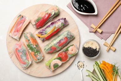 Delicious rolls wrapped in rice paper served on light table, flat lay