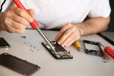 Photo of Technician repairing mobile phone at table, closeup