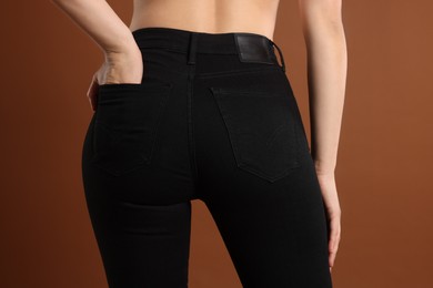 Photo of Woman wearing stylish black jeans on brown background, closeup