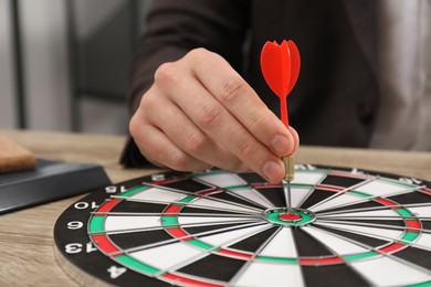 Business targeting concept. Man with dart aiming at dartboard at table indoors, closeup