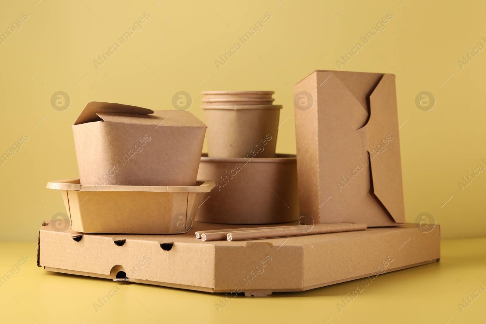 Photo of Eco friendly food packaging. Paper containers and tableware on pale yellow background