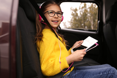 Photo of Cute little girl listening to audiobook in car