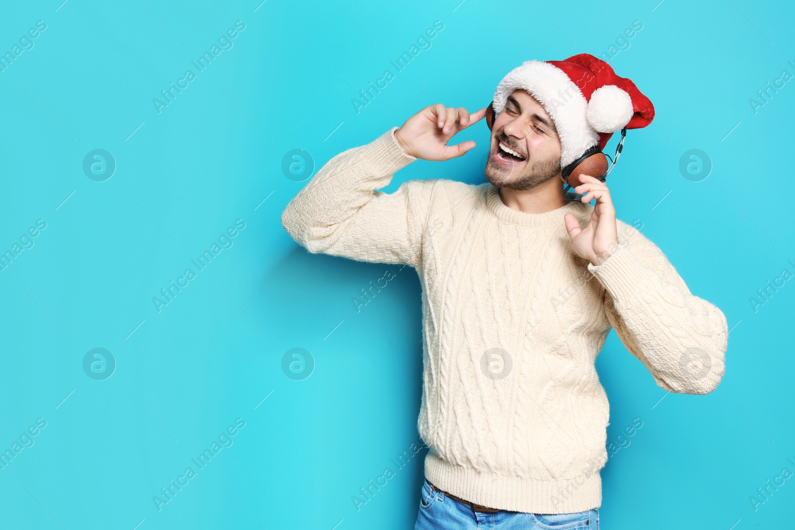 Photo of Young man in Santa hat listening to Christmas music on color background