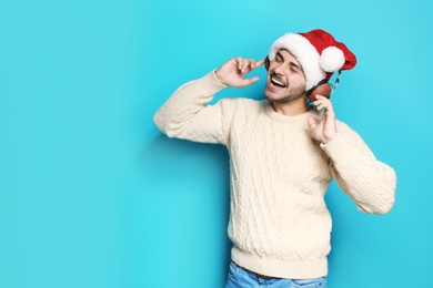 Young man in Santa hat listening to Christmas music on color background