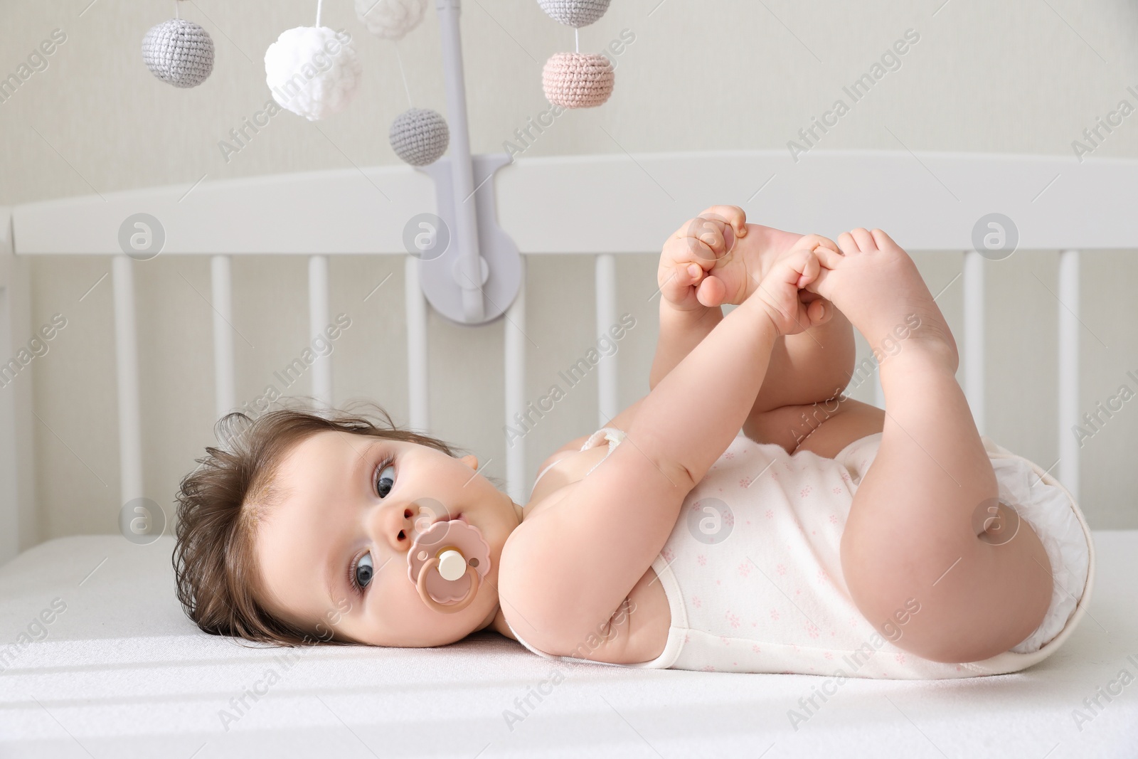 Photo of Cute little baby lying in crib with hanging mobile