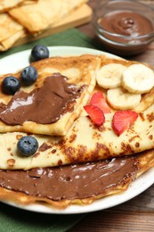 Photo of Tasty crepes with chocolate paste, banana and berries on wooden table, closeup