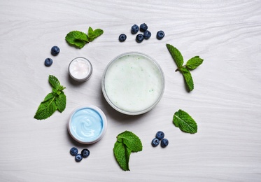 Flat lay composition with jars of body cream on light wooden background