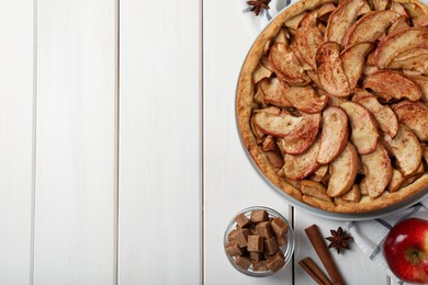 Photo of Delicious apple pie and ingredients on white wooden table, flat lay. Space for text