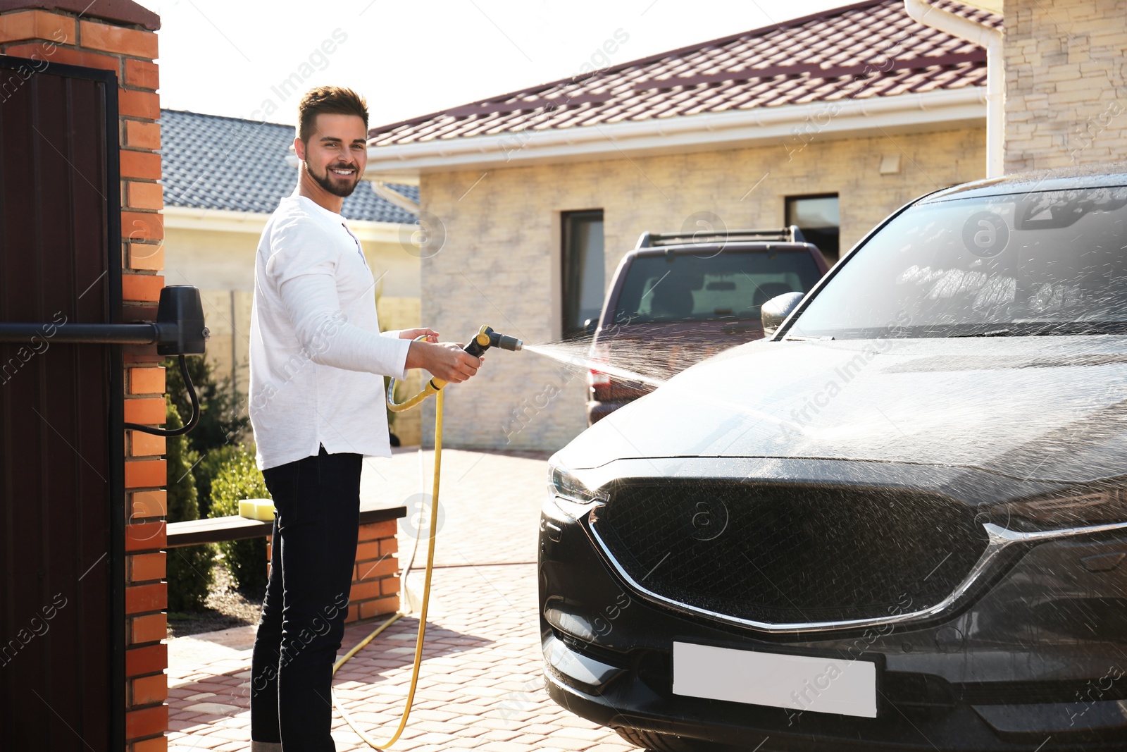 Photo of Young happy man washing car at backyard on sunny day