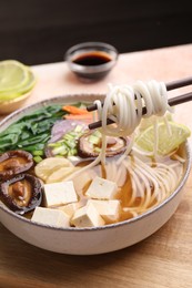 Photo of Eating delicious vegetarian ramen with chopsticks at table, closeup