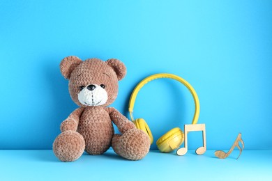 Photo of Baby songs. Toy bear, yellow headphones and wooden notes on light blue background