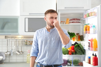 Man feeling bad smell from stale products in refrigerator at home
