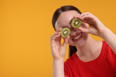 Photo of Smiling woman covering eyes with halves of kiwi on orange background, space for text