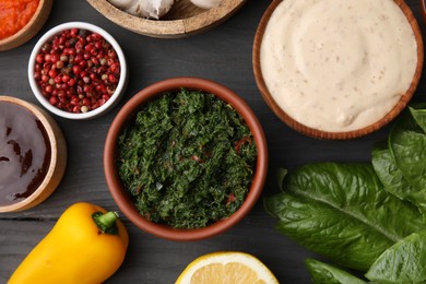 Different fresh marinades in bowls and ingredients on grey wooden table, flat lay