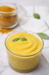 Photo of Tasty curry sauce, powder and basil leaves on white table, closeup