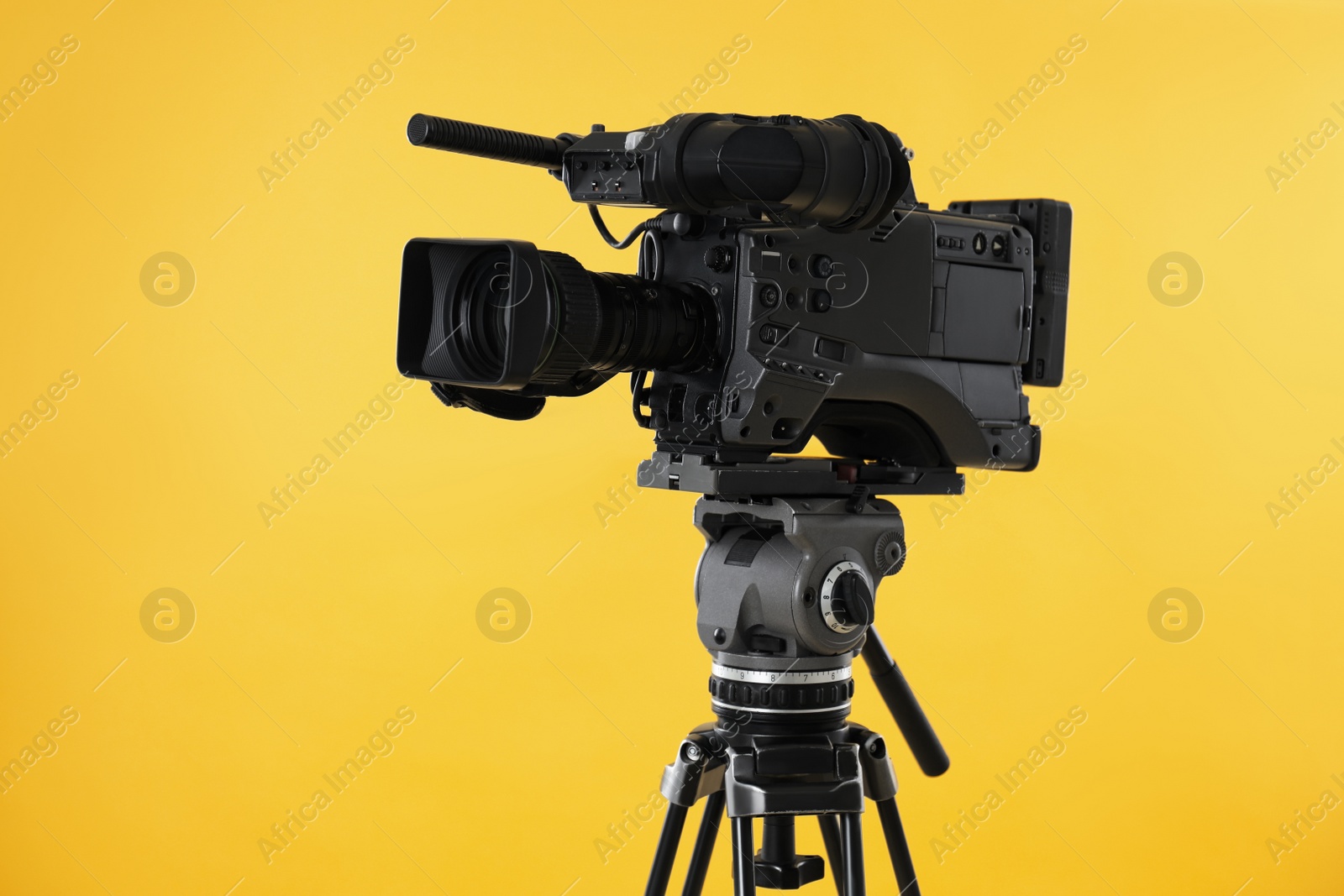 Photo of Modern professional video camera on yellow background