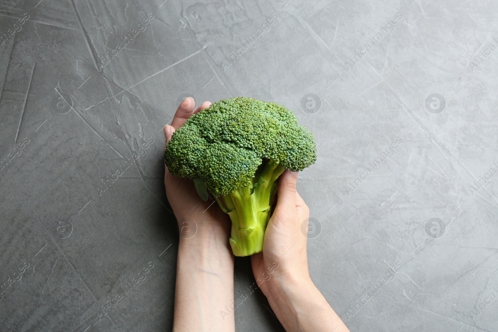 Photo of Young woman holding fresh broccoli over grey table, top view