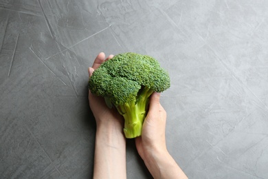 Photo of Young woman holding fresh broccoli over grey table, top view