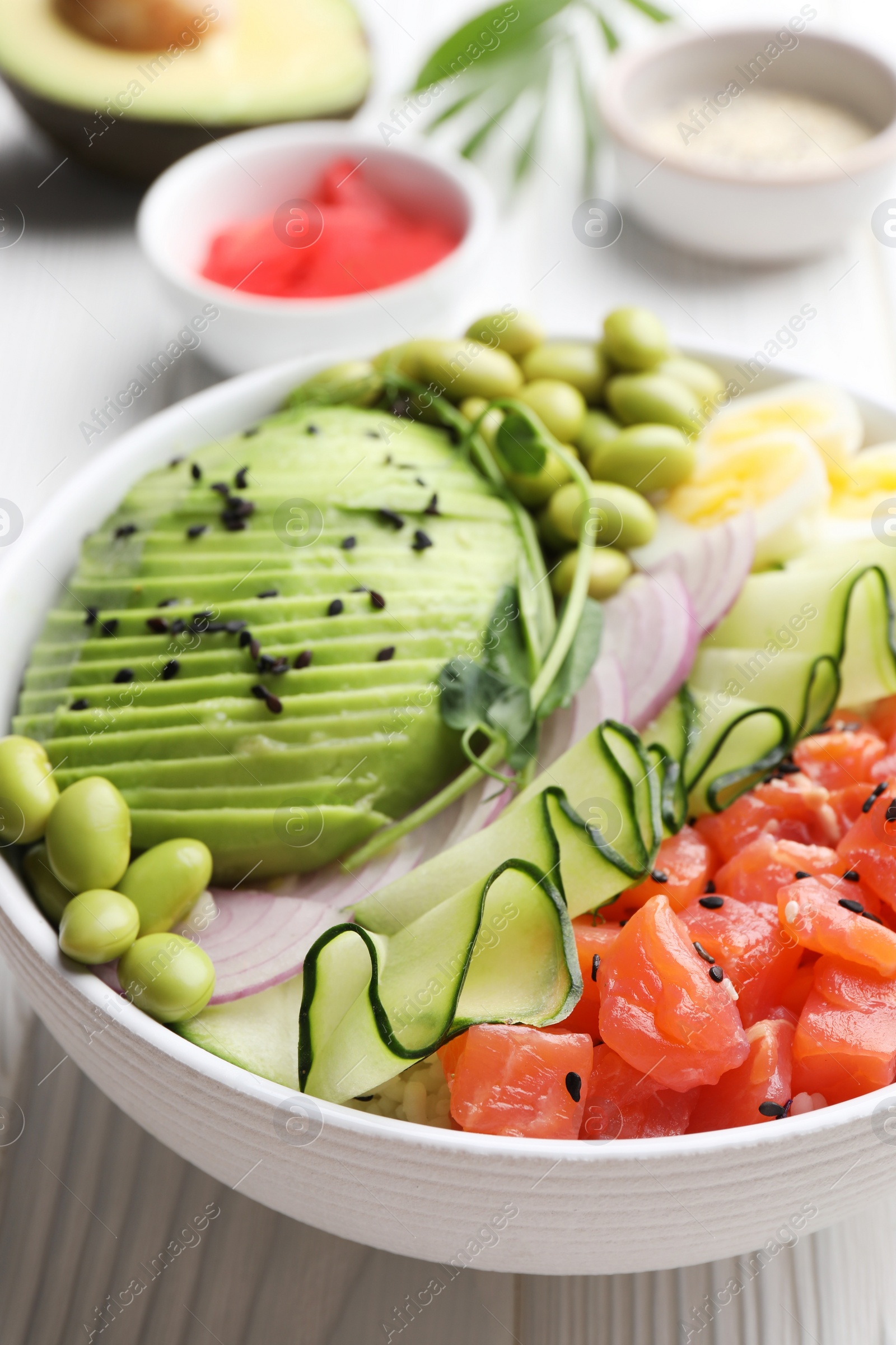 Photo of Delicious poke bowl with avocado, fish and edamame beans on white wooden table, closeup