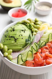 Delicious poke bowl with avocado, fish and edamame beans on white wooden table, closeup