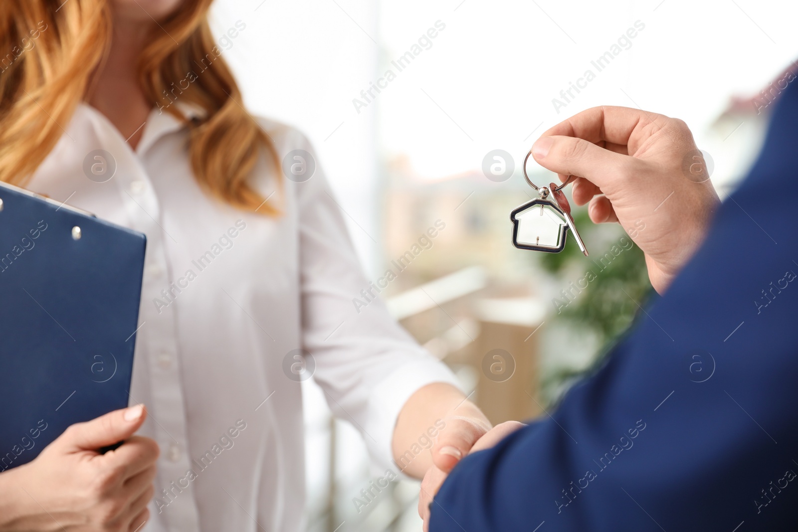 Photo of Real estate agent giving key with trinket to client in office, closeup