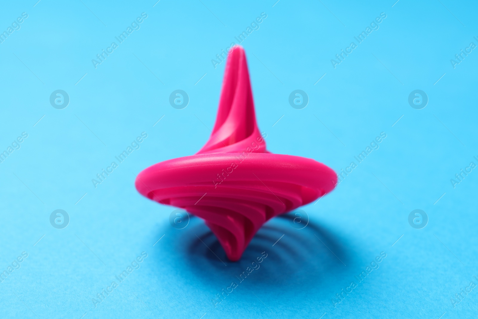 Photo of One pink spinning top on light blue background, closeup