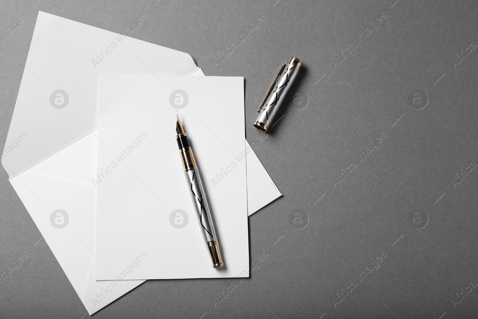 Photo of Blank sheet of paper, letter envelope and pen on grey background, top view. Space for text