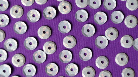Many silver sequins on purple background, flat lay