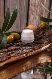 Glass jar of cream, olives and leaves on log near wooden wall