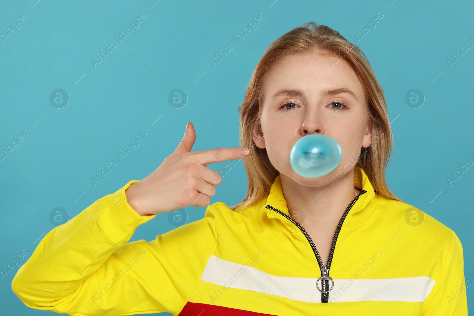 Photo of Beautiful young woman blowing bubble gum on light blue background