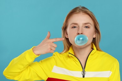 Beautiful young woman blowing bubble gum on light blue background