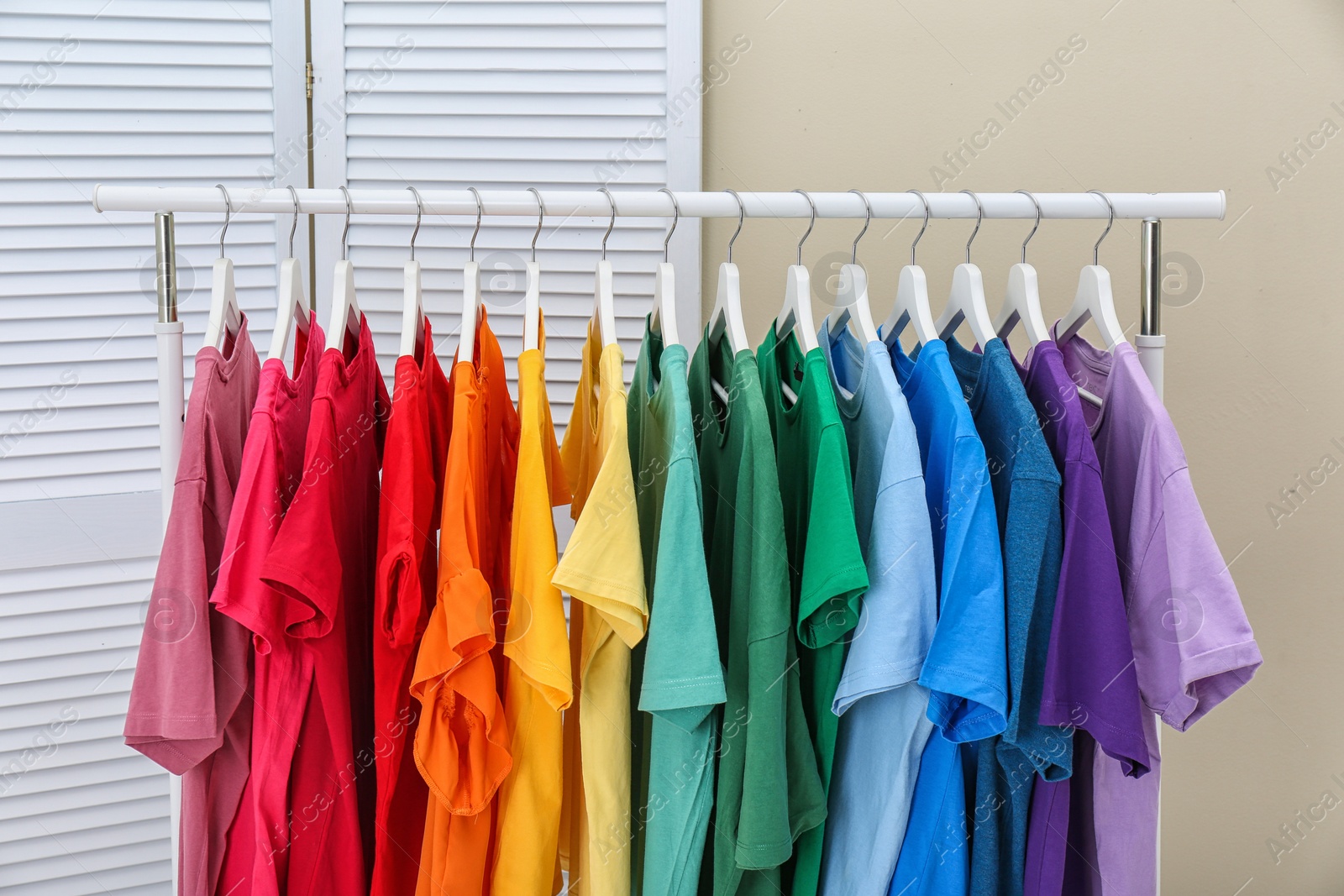 Photo of Rack with bright clothes in room. Rainbow colors