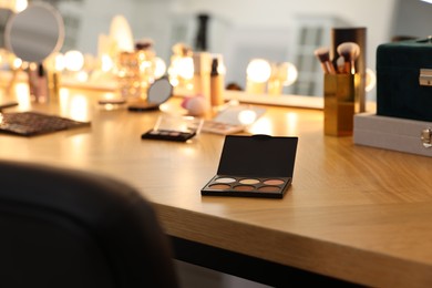 Photo of Eyeshadow palette and other cosmetic products on wooden dressing table in makeup room