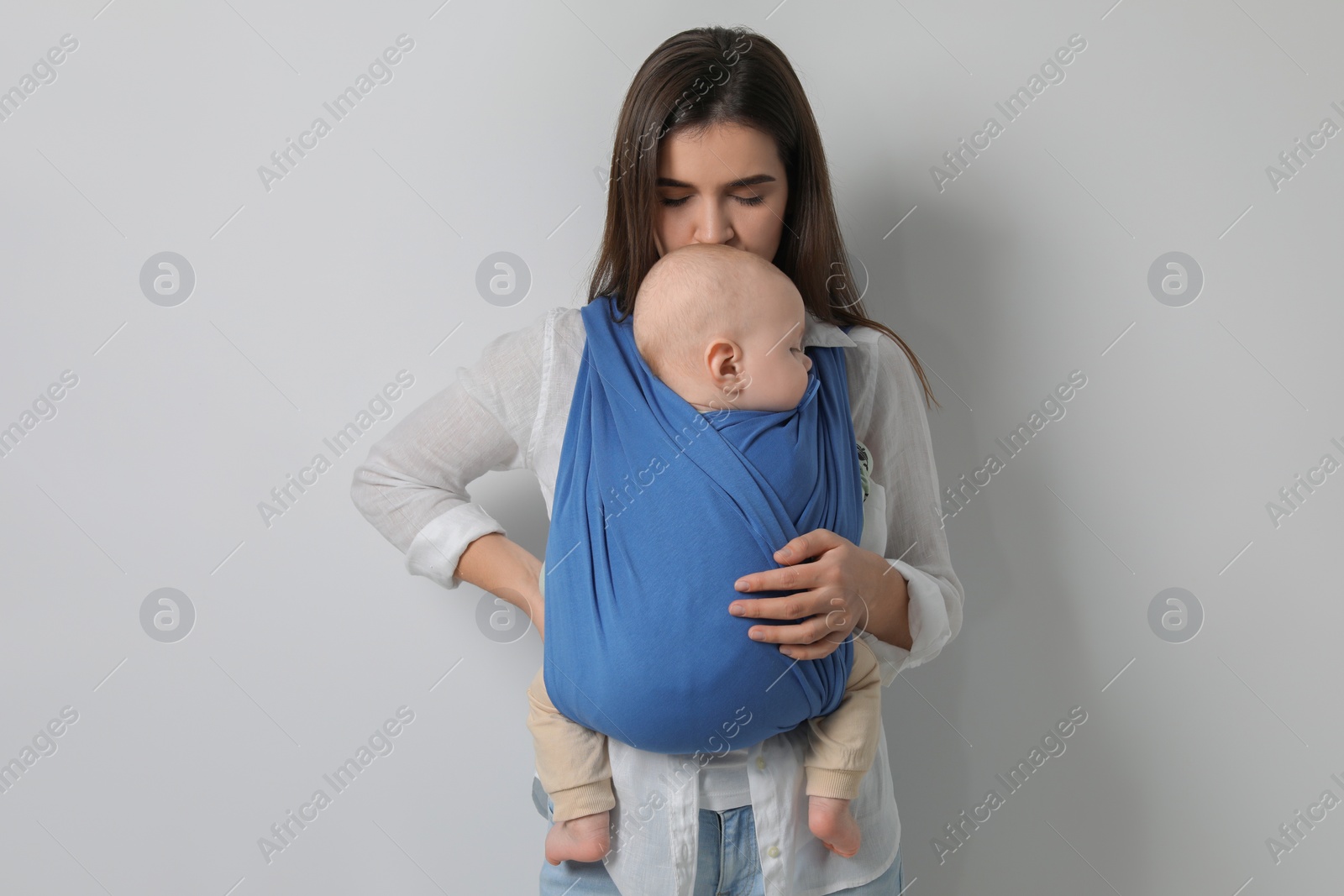 Photo of Mother holding her child in sling (baby carrier) on light grey background