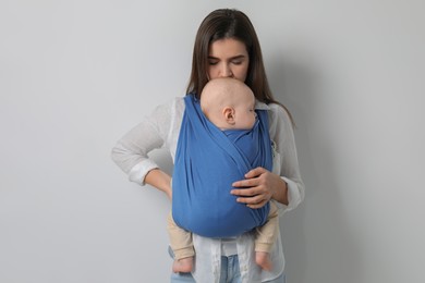Mother holding her child in sling (baby carrier) on light grey background
