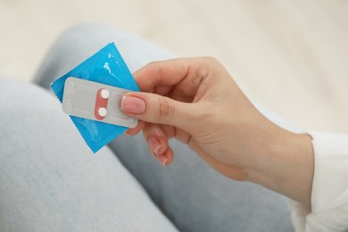 Photo of Woman holding condom and contraceptive pills, closeup. Choosing birth control method