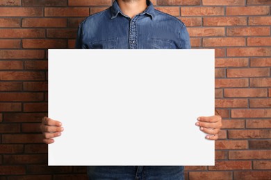 Photo of Man holding white blank poster near red brick wall, closeup. Mockup for design