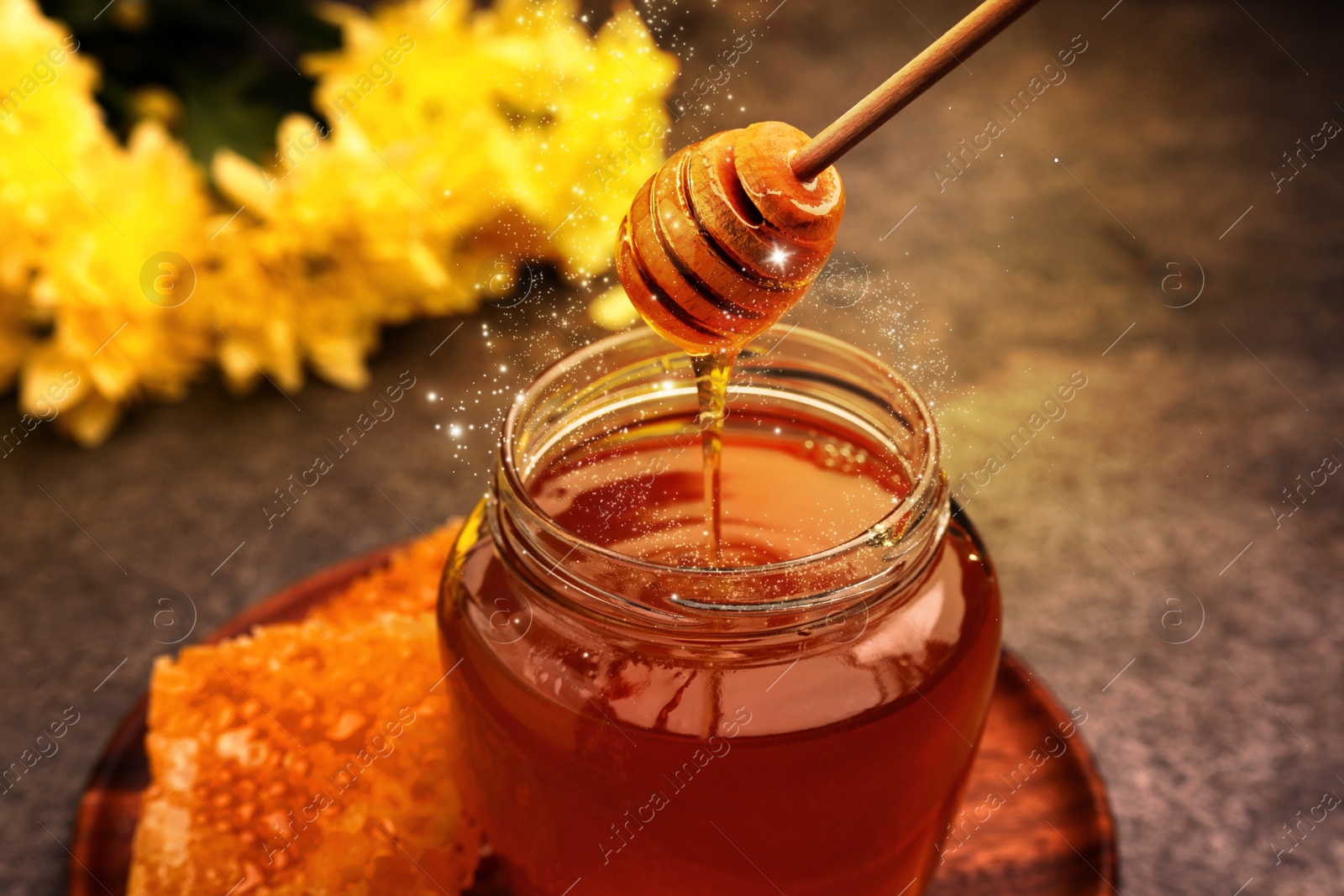 Image of Natural honey dripping from dipper into glass jar on table under sunlight, closeup