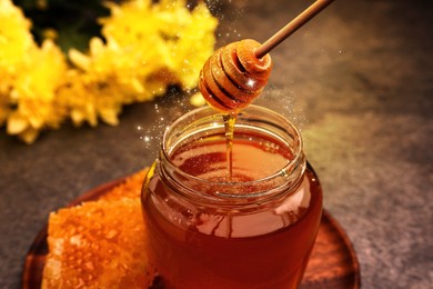 Natural honey dripping from dipper into glass jar on table under sunlight, closeup