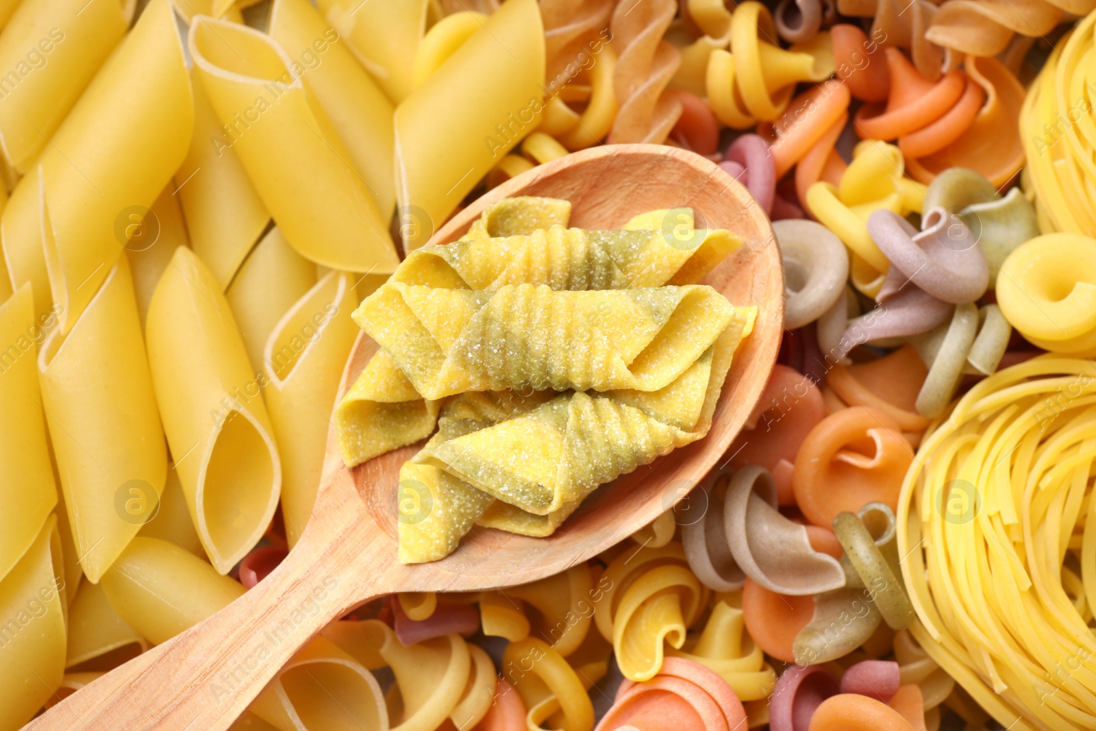 Photo of Wooden spoon and different types of pasta as background, top view