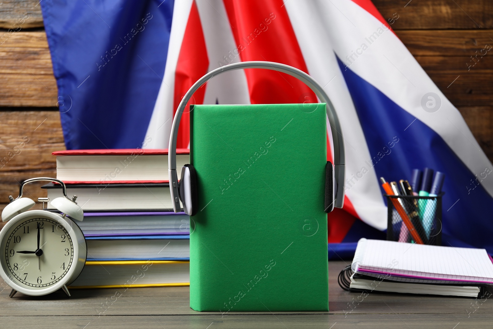 Photo of Learning foreign language. Different books, headphones, alarm clock and stationery on wooden table near flag of United Kingdom