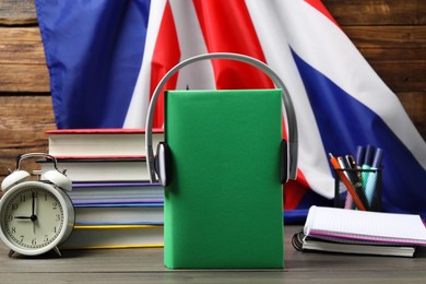 Learning foreign language. Different books, headphones, alarm clock and stationery on wooden table near flag of United Kingdom