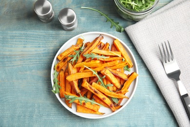 Plate with baked sweet potato slices and arugula served on wooden table, top view