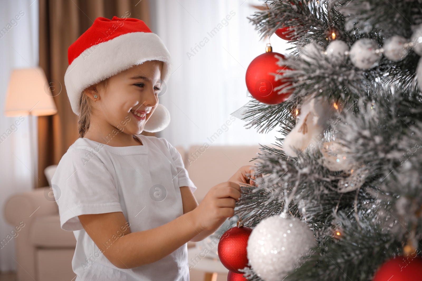 Photo of Cute little girl decorating Christmas tree at home