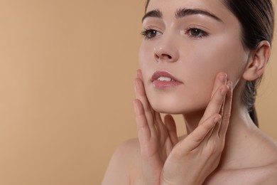 Young woman massaging her face on beige background. Space for text